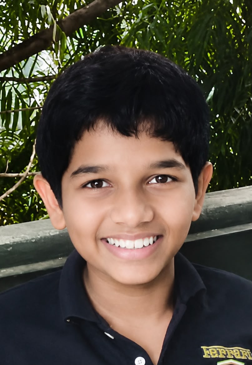 A smiling young boy (Dulmina Peiris) outdoors, surrounded by trees and greenery in 2016.